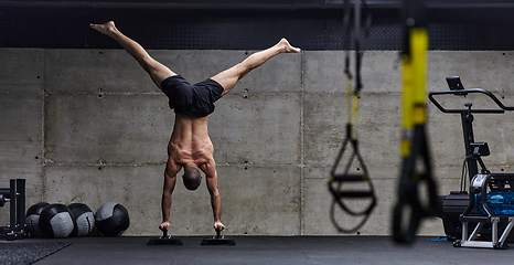 Image showing A muscular man in a handstand position, showcasing his exceptional balance and body control while performing a variety of exercises to enhance his overall body stability and strength in a modern gym