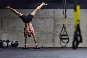 Image showing A muscular man in a handstand position, showcasing his exceptional balance and body control while performing a variety of exercises to enhance his overall body stability and strength in a modern gym