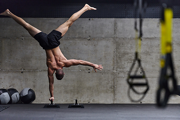 Image showing A muscular man in a handstand position, showcasing his exceptional balance and body control while performing a variety of exercises to enhance his overall body stability and strength in a modern gym