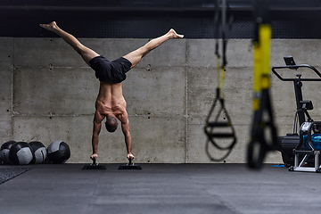 Image showing A muscular man in a handstand position, showcasing his exceptional balance and body control while performing a variety of exercises to enhance his overall body stability and strength in a modern gym