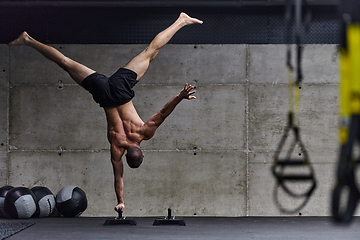 Image showing A muscular man in a handstand position, showcasing his exceptional balance and body control while performing a variety of exercises to enhance his overall body stability and strength in a modern gym