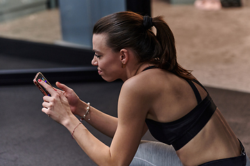 Image showing A fit woman in the gym taking a break from her training and uses her smartphone, embracing the convenience of technology to stay connected