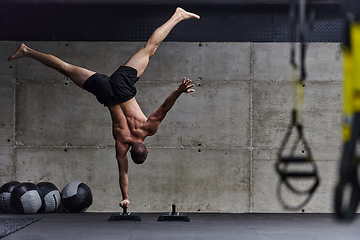 Image showing A muscular man in a handstand position, showcasing his exceptional balance and body control while performing a variety of exercises to enhance his overall body stability and strength in a modern gym