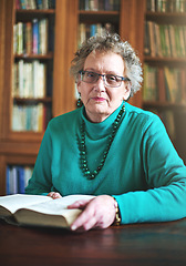 Image showing Getting in a great read. Portrait of a senior woman sitting at a table reading.