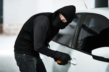 Image showing I think I heard someone coming. a masked criminal picking the lock of a car door inside a parking lot.