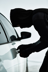 Image showing Weaving away until he breaks inside. a masked criminal picking the lock of a car door inside a parking lot.