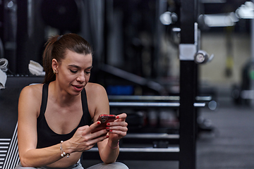 Image showing A fit woman in the gym taking a break from her training and uses her smartphone, embracing the convenience of technology to stay connected