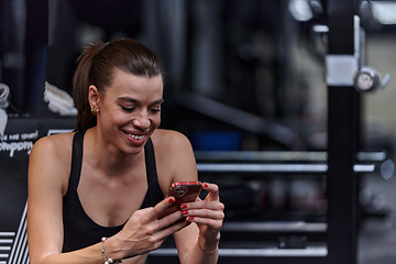 Image showing A fit woman in the gym taking a break from her training and uses her smartphone, embracing the convenience of technology to stay connected