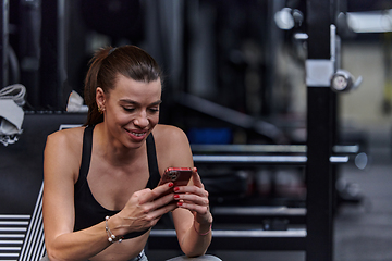 Image showing A fit woman in the gym taking a break from her training and uses her smartphone, embracing the convenience of technology to stay connected