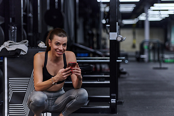 Image showing A fit woman in the gym taking a break from her training and uses her smartphone, embracing the convenience of technology to stay connected