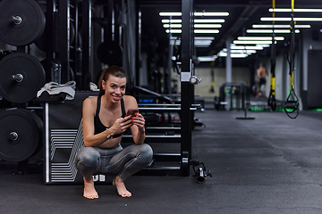 Image showing A fit woman in the gym taking a break from her training and uses her smartphone, embracing the convenience of technology to stay connected