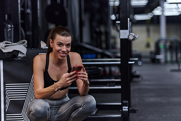 Image showing A fit woman in the gym taking a break from her training and uses her smartphone, embracing the convenience of technology to stay connected