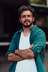 Image showing A successful young businessman in a shirt, with crossed arms, poses outdoors, confident expression on his face.