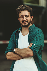 Image showing A successful young businessman in a shirt, with crossed arms, poses outdoors, confident expression on his face.