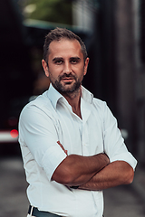 Image showing A successful businessman in a white shirt, with crossed arms, poses outdoors, confident expression on his face.