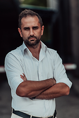 Image showing A successful businessman in a white shirt, with crossed arms, poses outdoors, confident expression on his face.