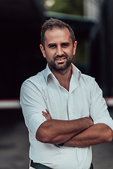 Image showing A successful businessman in a white shirt, with crossed arms, poses outdoors, confident expression on his face.