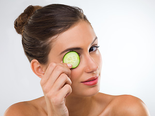 Image showing Eye treatment, homestyle. Portrait of a gorgeous young woman holding a slice of cucumber over her eye.