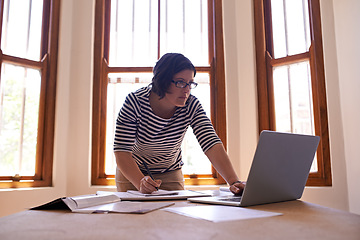 Image showing Hard work always pays off. A cropped shot of a woman standing at her desk and working on her laptop.