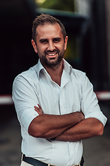 Image showing A successful businessman in a white shirt, with crossed arms, poses outdoors, confident expression on his face.