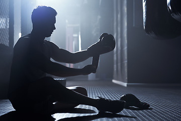 Image showing Gearing up for some powerful punches. a sporty young man strapping his gloves while boxing in a gym.