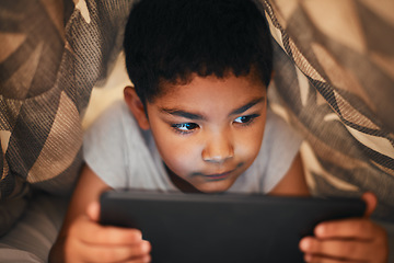 Image showing Hes too curious to sleep. an adorable little boy using a digital tablet while lying under a blanket at home.