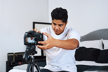 Image showing I have to get the perfect angle. a young man using a camera on a tripod to record himself at home.