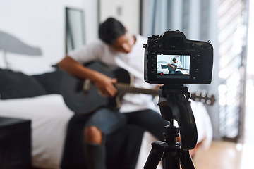 Image showing Im doing another cover. a young man recording himself at home while playing the guitar.