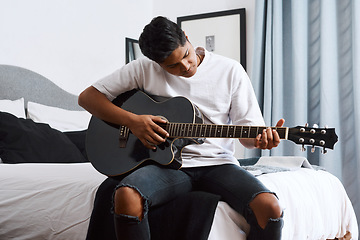 Image showing Im playing my favourite song. a young man playing the guitar while sitting at home.
