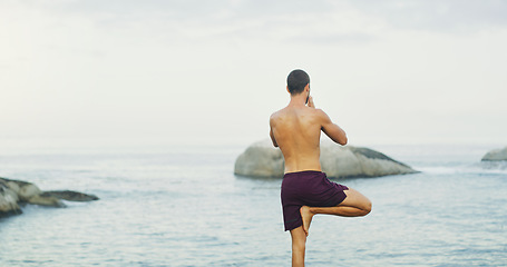 Image showing Quiet the mind and the soul shall speak. Rearview shot of an unrecognizable man standing and doing yoga alone by the ocean during an overcast day.