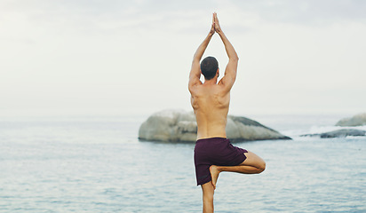 Image showing Yoga is the science of well being. Rearview shot of an unrecognizable man standing and doing yoga alone by the ocean during an overcast day.