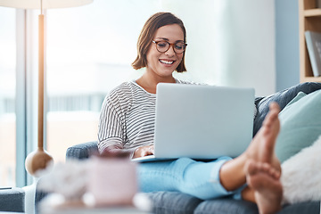 Image showing She cant hide the blush on her face. Full length shot of a happy young woman using a laptop while relaxing in her living room.