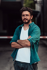 Image showing A successful young businessman in a shirt, with crossed arms, poses outdoors, confident expression on his face.