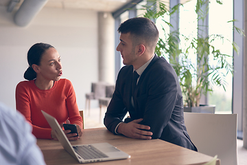 Image showing A young entrepreneurial couple sits together in a large, modern office, engaged in analyzing statistics and data on their laptop