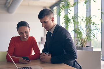 Image showing A young entrepreneurial couple sits together in a large, modern office, engaged in analyzing statistics and data on their laptop