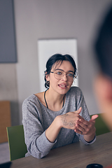 Image showing In a modern office, a young smile businesswoman with glasses confidently explains and presents various business ideas to her colleagues, showcasing her professionalism and expertise.