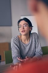 Image showing In a modern office, a young smile businesswoman with glasses confidently explains and presents various business ideas to her colleagues, showcasing her professionalism and expertise.
