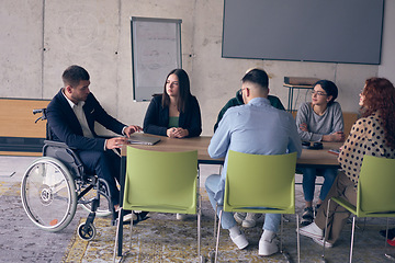 Image showing A diverse group of business professionals, including an person with a disability, gathered at a modern office for a productive and inclusive meeting.