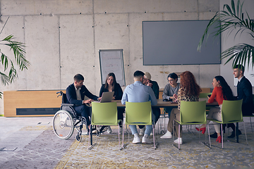 Image showing A diverse group of business professionals, including an person with a disability, gathered at a modern office for a productive and inclusive meeting.