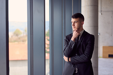 Image showing The confident businessman in a sleek suit strikes a pose, exuding charisma and professionalism, amidst the modern ambiance of the office.