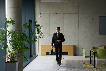 Image showing A confident businessman with a briefcase strides through a modern office, exuding charisma and determination, symbolizing success and professional excellence.