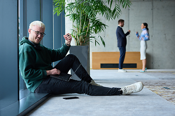 Image showing A young blond man in a modern office sits by the window, engrossed in his work on a laptop