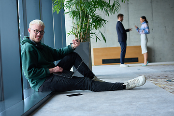 Image showing A young blond man in a modern office sits by the window, engrossed in his work on a laptop