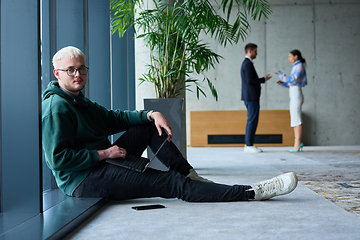 Image showing A young blond man in a modern office sits by the window, engrossed in his work on a laptop