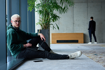 Image showing A young blond man in a modern office sits by the window, engrossed in his work on a laptop