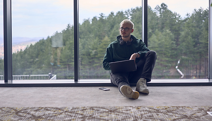 Image showing A young blond man in a modern office sits by the window, engrossed in his work on a laptop