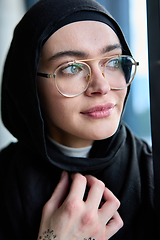 Image showing A hijab businesswoman stands by the window in a modern office holding a tablet in her hand showcasing her professionalism, technological prowess and entrepreneurial spiri