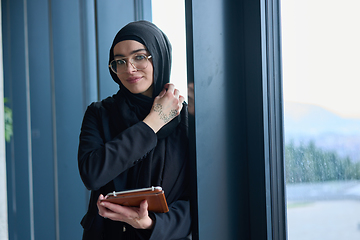 Image showing A hijab businesswoman stands by the window in a modern office holding a tablet in her hand showcasing her professionalism, technological prowess and entrepreneurial spiri