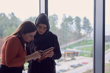 Image showing In a modern office a pair of colleagues, one wearing a hijab, engage in a lively discussion, sharing their business ideas and fostering a diverse and inclusive work environment.