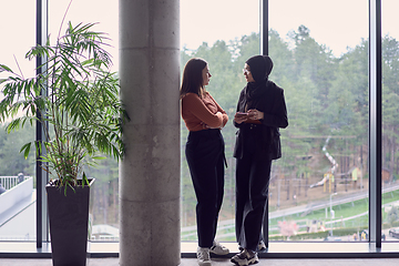 Image showing In a modern office a pair of colleagues, one wearing a hijab, engage in a lively discussion, sharing their business ideas and fostering a diverse and inclusive work environment.